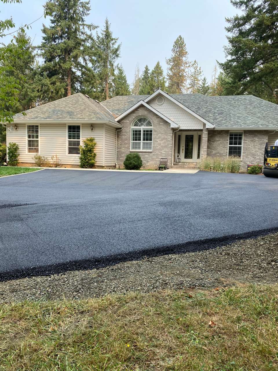 Freshly paved black asphalt driveway in front of a single-story stone and siding home