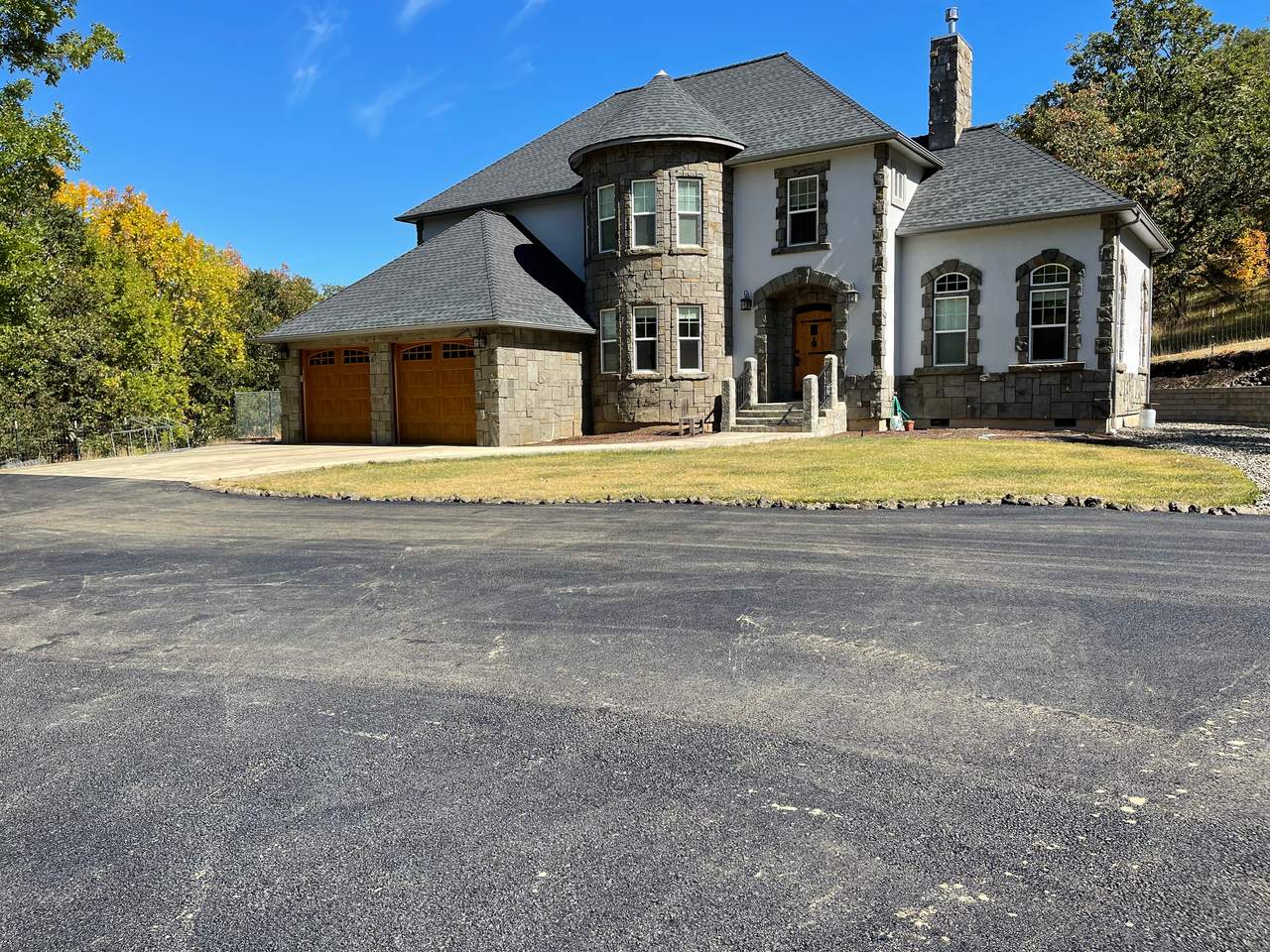 Wide new asphalt driveway and turnaround in front of a two-story stone house with a turret