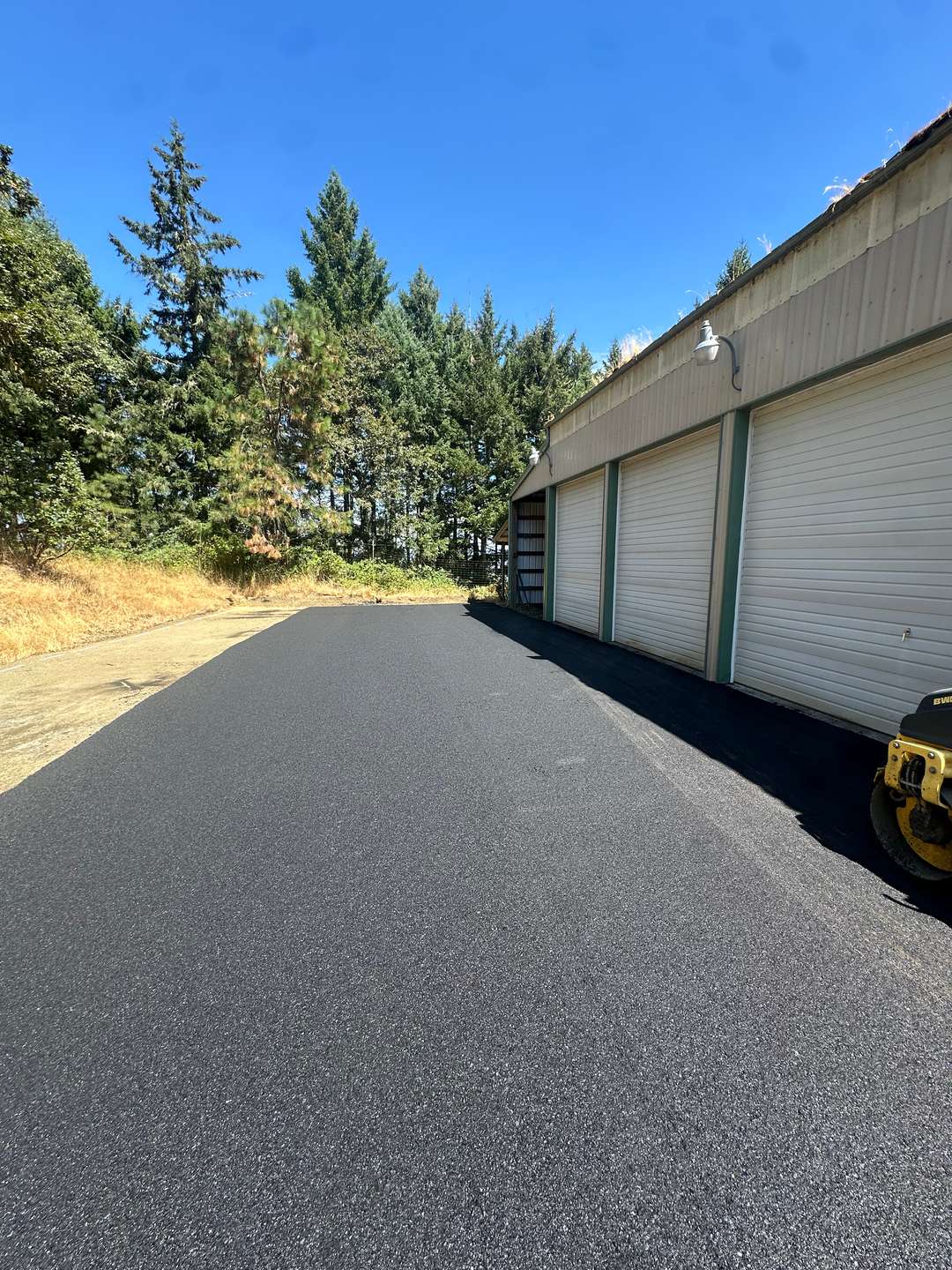 New asphalt apron along a row of garage doors, a small roller at the edge