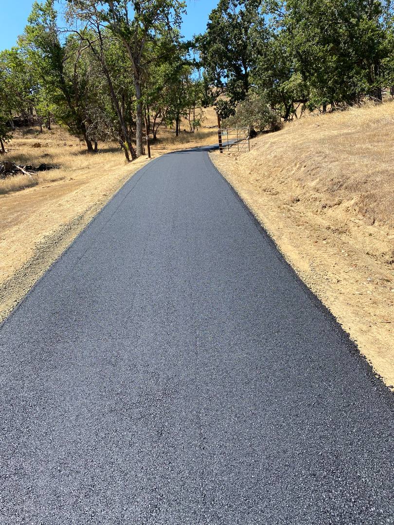 Long new asphalt lane with crisp edges running between dry grass and oak trees