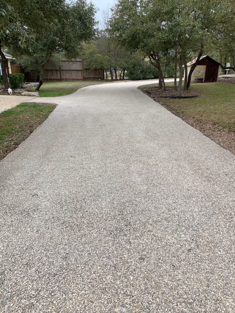 Long chip seal driveway with a coarse stone texture, lined by trees and lawn