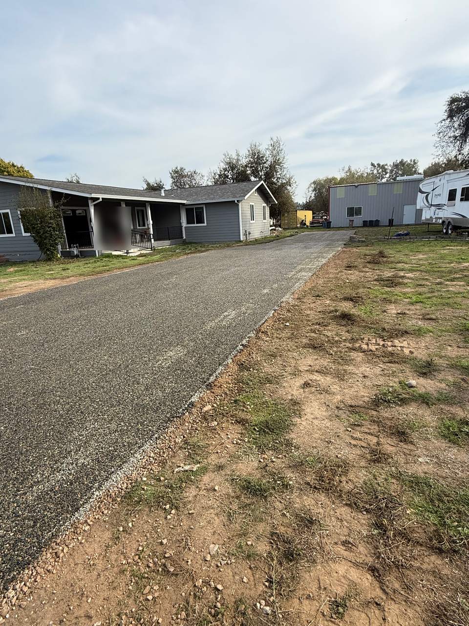 Chip seal driveway with a fresh stone surface running past a gray single-story home
